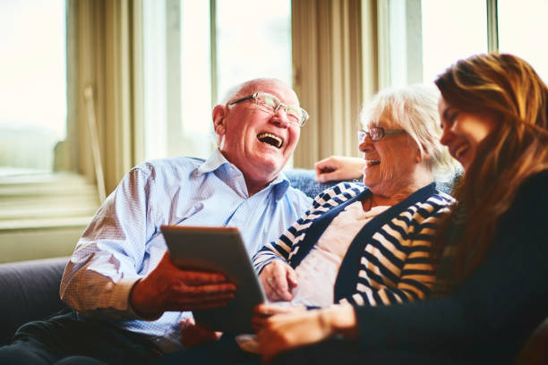 An older couple laughing with a younger woman over a tablet