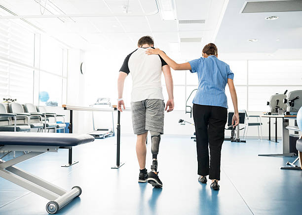 A physiotherapist supporting a young man with a prosthetic leg in a rehabilitation gym